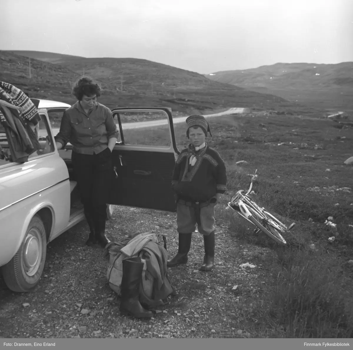 Jenny Drannem står ved siden av familiens bil på Rv98, Ifjordfjellet. En ukjent gutt iført sameklær står ved siden av.