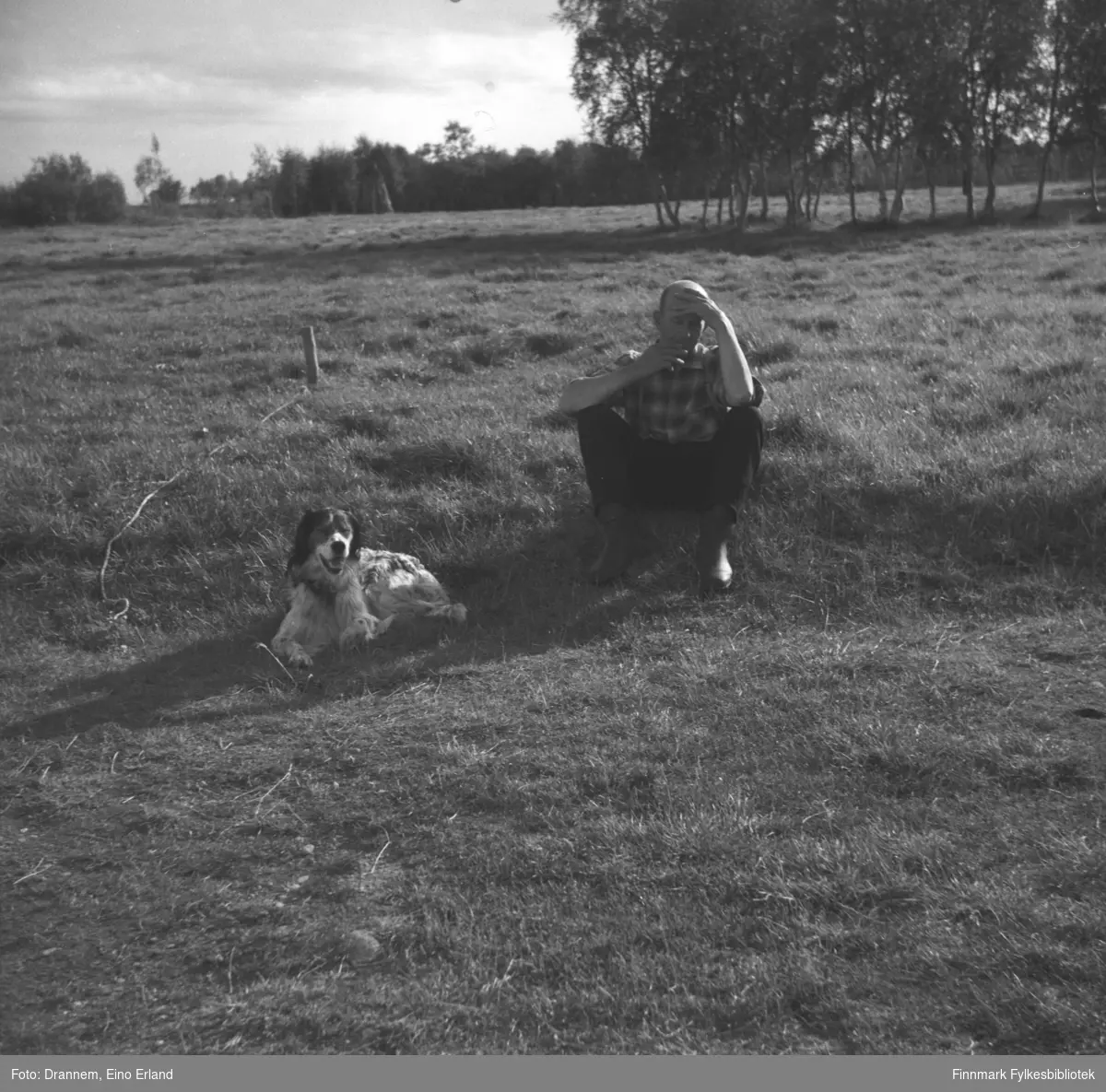 Uuno Lappalainen sitter på et jorde med hunden Rexi ved siden av seg. Stedet er ukjent.