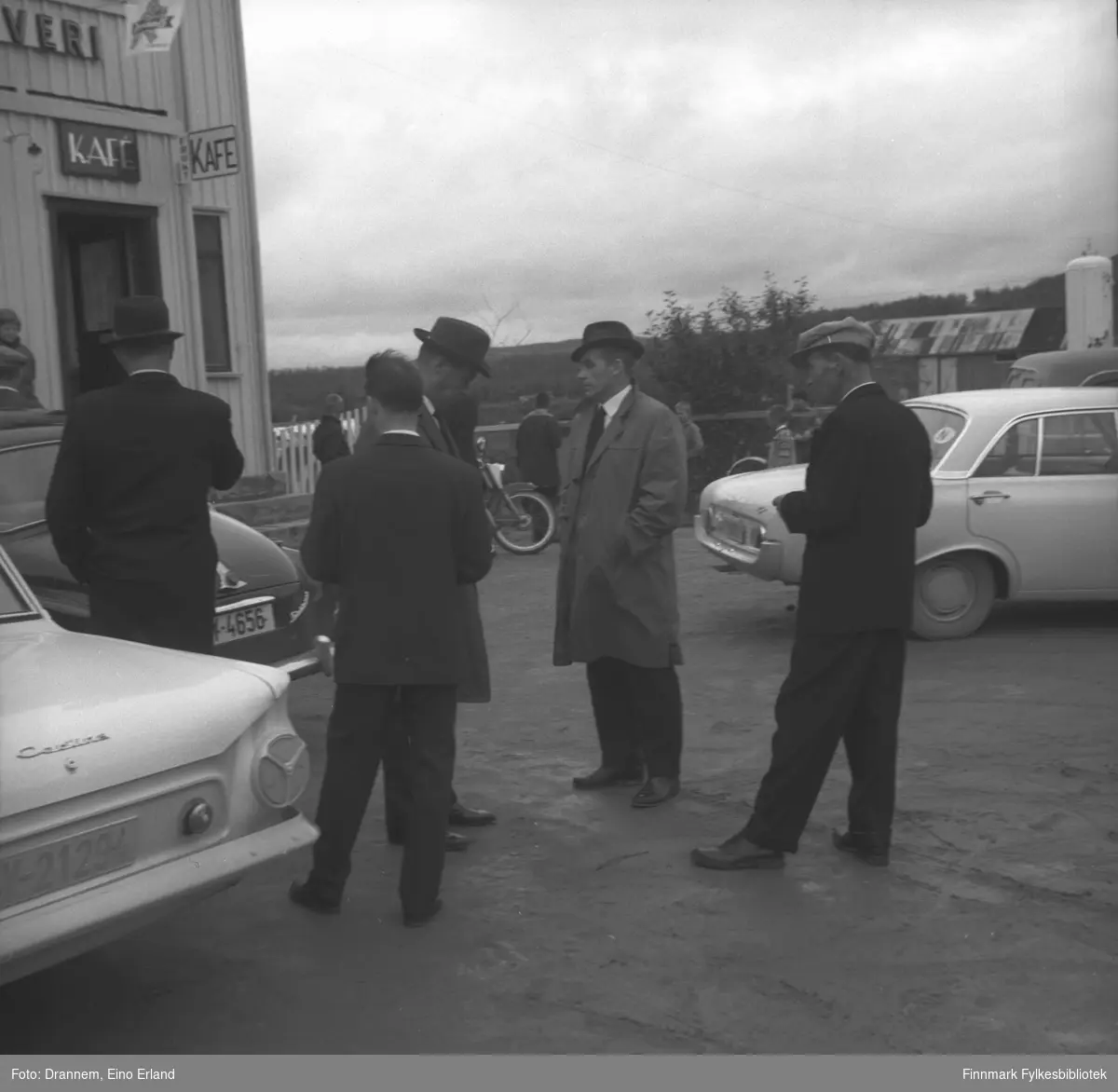 Fem dresskledte menn står på en parkeringsplass utenfor en kafe i Neiden. Bilene er fra venstre: Ford Cortina (Y-21294), Skoda Octavia (Y-4656) og Ford Taunus 17M 1961-62.