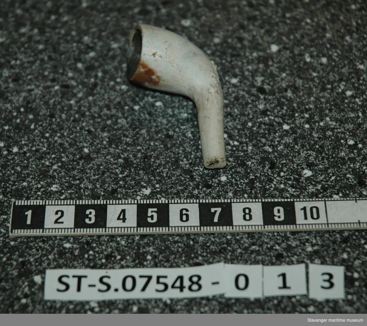 Krittpipehode med fragment av stilk. Funnet i sjakt 2. Dekorert på undersiden med løvblad-lignende utskjæring. Funnet på ca. 30cm dybde.