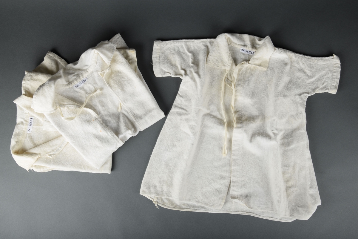 Tre hvite babykjortler. Kjortlene har knytting ved kragen og korte ermer.