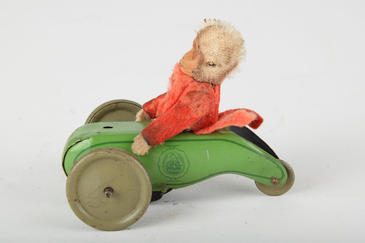 Mekanisk leketøy av en lekebil med apekatt i tøy som sjåfør. Mekanikken har trolig drevet hjulakslene rundt.