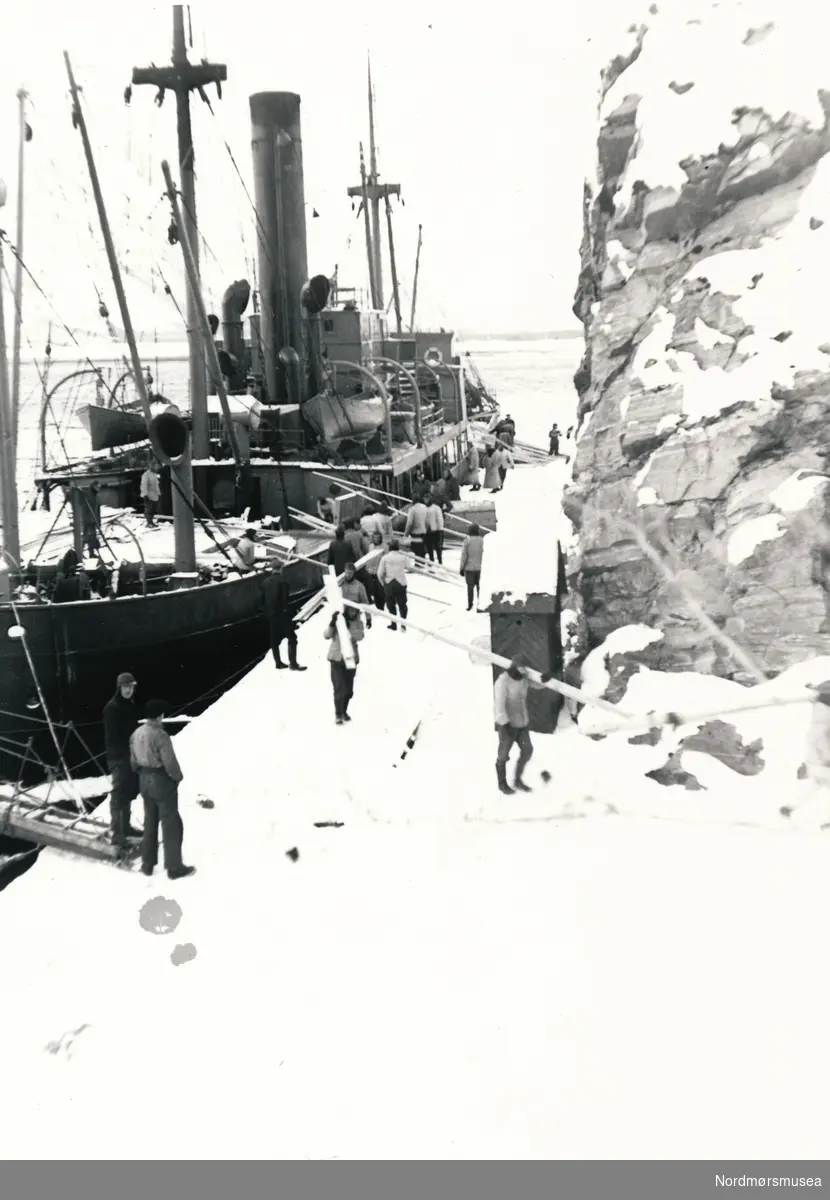 Her ser vi ein båt som ligger til kai ved Hammarkaia. Soldater og arbeidsfolk på kaia som laster av skipet.