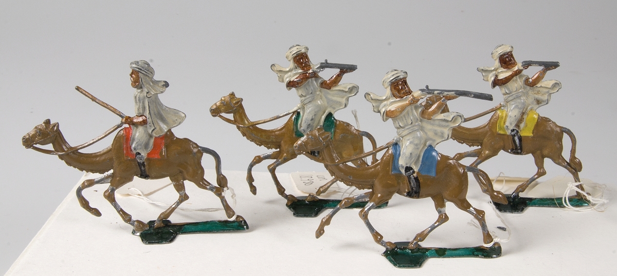 Fyra tennsoldater föreställande "beduinskyttar" i vita kläder ridande på ljusbruna kameler.