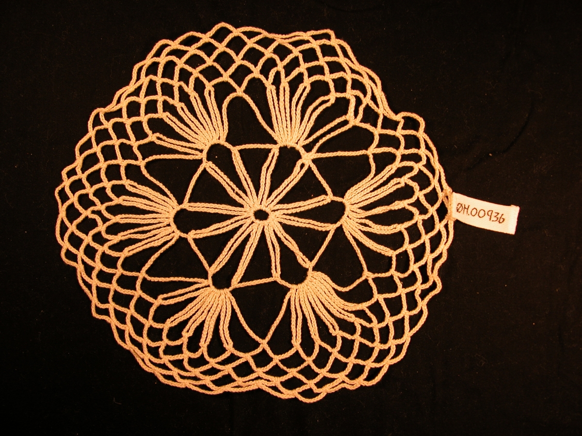 12 par "stavar" som heng fast i ein sirkel i sentrum. Kvart par er bunde til edet neste par ved hjelp av ein boge. Ut frå desse bogane dannar 5 stavar eit hand-liknande mønster. Kanten har eit rutemønster.