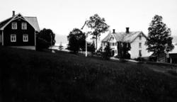 To trebygninger, 
med en bil, og flaggstang. (Fra Nordmøre M