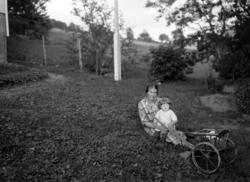 Foto av et lite barn sittende på fanget til sin mor utenfor 