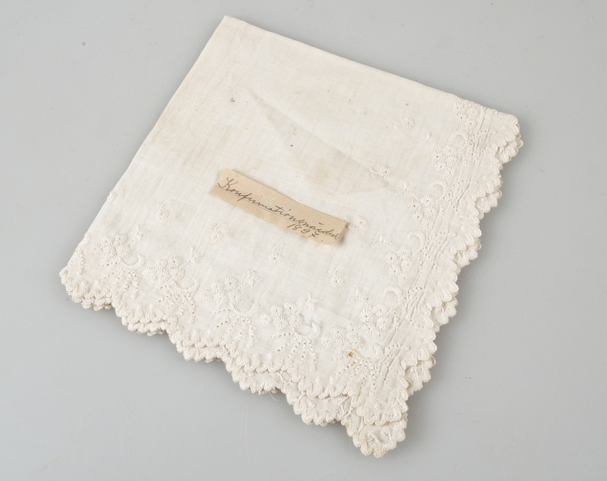 Konfirmationsnäsduk av bomullslärft med engelskt broderi. Gulnad påklistrad lapp med text: Konfirmationsnäsduk 1897.
