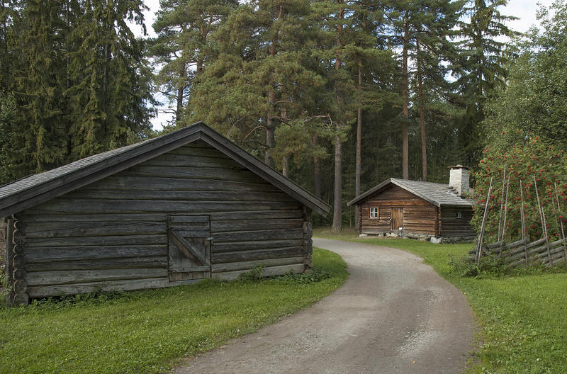 A road of sand and pebbles lead in between teo traditional log cabins in the open air museum.