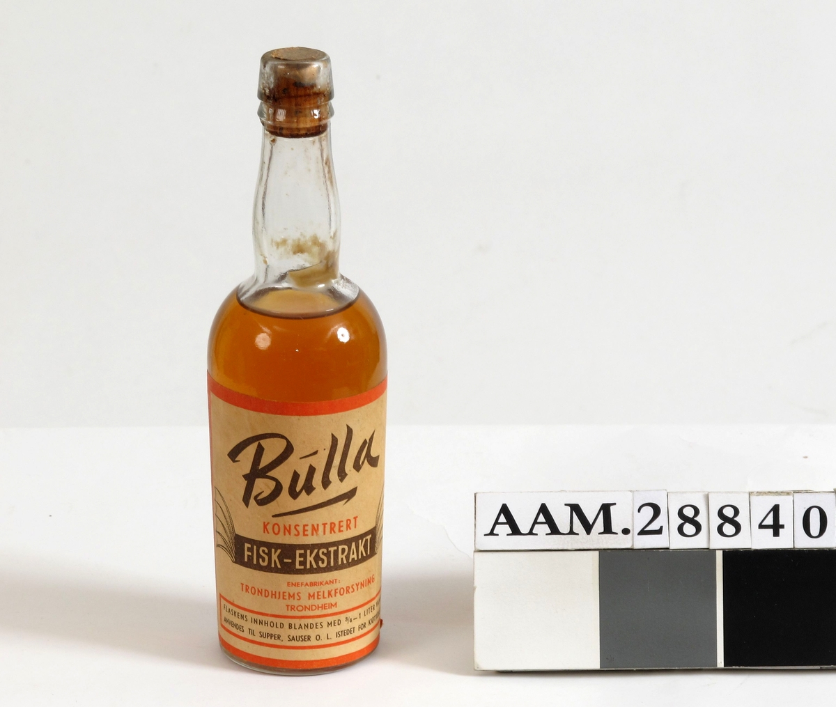 Flaske med kork og originalt innhold. Etikett med tekst, Bulla konsentrert fiskeekstrakt, produsert i Trondheim som krisevare, Brukes istedet for kjøttkraft. 