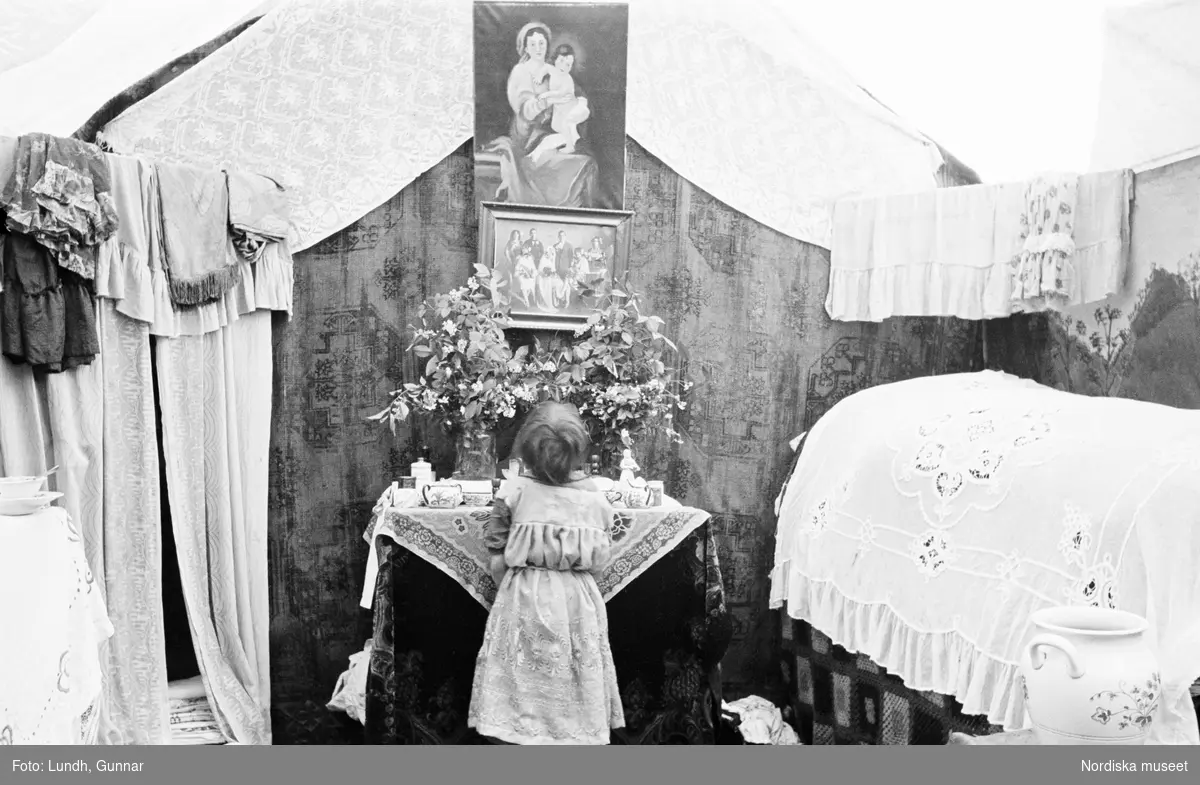 Interiör från familjen Taikons läger vid Johanneshov, södra Stockholm. Liten flicka ber vid familjens altare. Ovanför på väggen en bild av madonnan med barnet och ett familjefotografi.