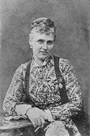 Porträttfoto av Christina Nilsson. Hon bär en mönstrad blus samt har smycken och medaljer på bröstet.