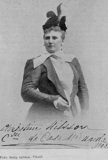 Foto av Christina Nilsson iförd promenaddräkt och hatt. Under bilden en autograf: "Christine Nilsson, Ctesse de Casa Miranda, 1905".
