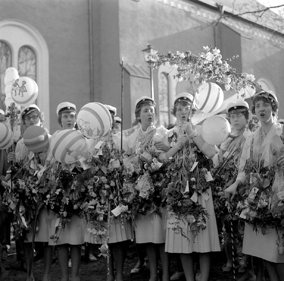 Studenterna, tredje d. 1960. 
Några kvinnliga studenter sjunger i väntan på talet vid Esaias Tegnérs 
staty. I bakgrunden skymtar domkyrkan.