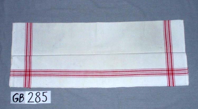 Handduk. Handvävd.
Varptäthet: 10 tr/cm.
Fållar: 0,5 cm, maskinfållade.
Hängband: handvävda, 0,8 cm breda, 
7 cm långa, vita.
Varpordning till bård:
Rött:     2 7 3 7 2
Oblekt:  4 4 4 4
Inskrivet i huvudkatalogen 1996-1997.