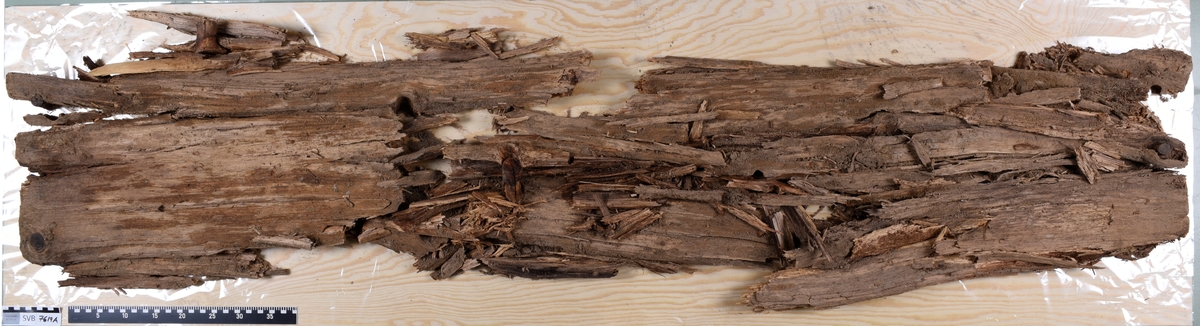 Deler av en rektangulær gravkiste. Det er kistebunnen, kistelokk, kistesidevegger og deler av hodeendegavlen.
Kistelokket er laget av et flatt og rektangulært bord som er laget av ett stykke tre. Bordet er sterkt fragmentert.
Kistesidene er i litt bedre tilstand. Bordene er avlange, rektangulære og laget av et stykke tre hver. Bordene ble festet med spiker til kistebunnen. Det er en spiker igjen i venstre sideveggen. Begge sidebordene har langsgående sprekker og er delvis brudd i flere deler.
Kistebunnen er laget av et flatt og rektangulært bord som er laget av ett stykke tre. Det er flere langsgående sprekker og flere kvisthull. Fargen er mørk brun med enkelte lysere brune partier i hodeenden.  I begge kortender er det rester etter hodegavlen og fotendegavlen og langs venstre siden er det rester etter kisteveggen. Hodeenden er bredere enn fotenden.
Hodeendegavlen er laget av en tykkere rektangulær trekube. Den har brudd opp i flere deler både på grunnen av nedbrytingen og under utgravningen.