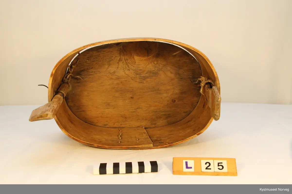 Oval utforming. Laupen har lokk som er innfelt i to trestykker som er festet i siden på laupen, hvor det ene trestykket er dreibart, og utgjør feste for lokket.