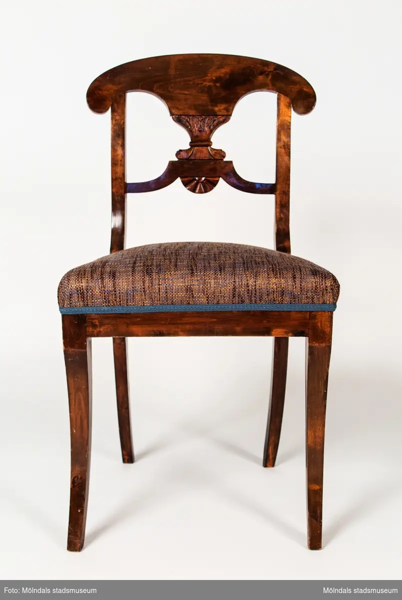 Stol tillverkad av betsad björk. Övre delen av ryggen är utformad som en pelta som bärs upp av ett akantusliknande ornament som i sin tur vilar på en konturerad tvärslå. Under dena finns ett solfjäderonament. De fristående benen är sabelformade. Stoppad fast sits.
På baksargens insida är stolen brännstämplad CALAS.
Denna modell tillverakdes i tämligen stor omfattning i Lindome på 1820-30-talen.