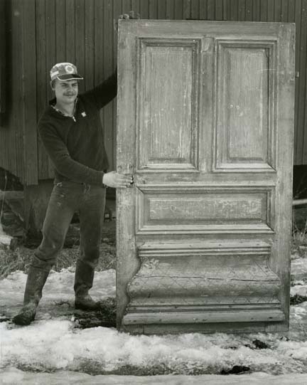 En man står och poserar intill en spegeldörr. Fotografiet är taget utomhus i Forneby.