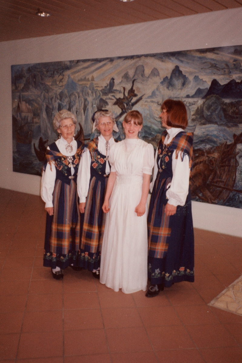 Jente i konfirmasjonskjole og tre kvinner i bunad, inne i Kulturhuset.