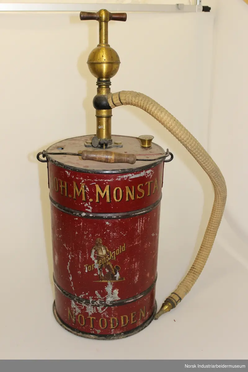 Et rødt sylinderformet brannapparat med messing håndtak og beige slange
Markert: "Joh.M.Monstad"