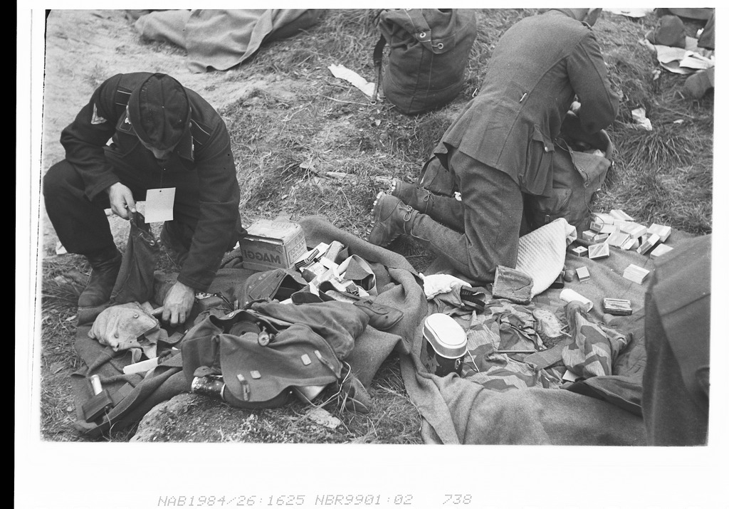 Tysk millitærleir etter frigjøringen. Engelsk soldat kontrollerer om den tyske soldaten prøver å få med seg hjem noe av verdi. Ser ut som det er ved Rafaelsen elva?