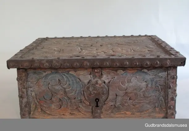 "Bladformer, smøygde band og drageornamentikk. Millom kantjarn og utskurden hev lokket fint utskorne små blad og halvrunde aggar. Vel vedlikehalde, sterk jarning og prydelege gangjarn. Truleg frå 1500 talet. Fra Haugen, Øystre Gausdal". (Jf. "Katalog for Lom Bygdesamling,1925).
Skrinrammen er holdt sammen av utvendige hjørnekantbeslag; jernhandtak i hver side. Fronten har nøkkelhullslås med beslag rundt. Lokket er satt samen av 2 bord, forsterket med jernbeslag rundt kanter på overside; to hengselbeslag festet til innside av lokk og bakstykke. Skrinsider blir holdt sammen av beslag ned langs hjørnekanter; har jernhandtak festet på jernbeslag.
Bunnen er satt sammen av 2 bord, festet til hverandre med to forsenka treplugger; bunnen var opprinnelig festet til underkant av skrinsider med 4 x 4 trenagler,seinere festet med spiker. 
Det er jernbeslag  på bakstykket midt, rundt hjørnekanter, omkring nøkkelhullslås, rundt lokk samt 2 handtak med beslag. Alle beslag er festet med store jernnagler; beslag på sidestykker er festet med små jernnagler under skrinbunnen. 3 av 8 bunnfester for beslag er fortsatt intakte.
DEKOR. De store jernnaglene med forskjøvet plassering på beslag ble sannsynligvis brukt som dekorelement; runde beslag på sider, bakstykke og front. Flatskurd på lokk med flettet, stilisert renessanseranke, der bladverk er "omgjort" til småspiraler eller rundinger.  På skrinsidene akantusskurd med c-former, bladtunger uten stilk og naturalistiske småblad i rokokkostil. Flatskurd var vanlig i Gudbrandsdalen i perioden ca. 1650-1750, mens akantusmotivet først ble vanlig på bruksgjenstander i løpet av siste halvdel av 1700-tallet. Den mørkere grønne og blå dekorfargen var vanlig i siste del på 1700-tallet; den brune bunnfargen var vanlig i bruk fra 1780-tallet. 
BRUK. Før kofferten kom i bruk hadde man reiseskrinet, som ble brukt til oppbevaring av bl.a. klær, verdisaker og mat på reiser. Skrinet hadde ofte et eller to mindre, smale rom langs den ene skrinsiden og ett større rom. De fleste reiseskrin var i tillegg forsterket med jernbeslag langs alle kanter og med en solid nøkkelhullås til sikring mot støt, slag og tyveri.