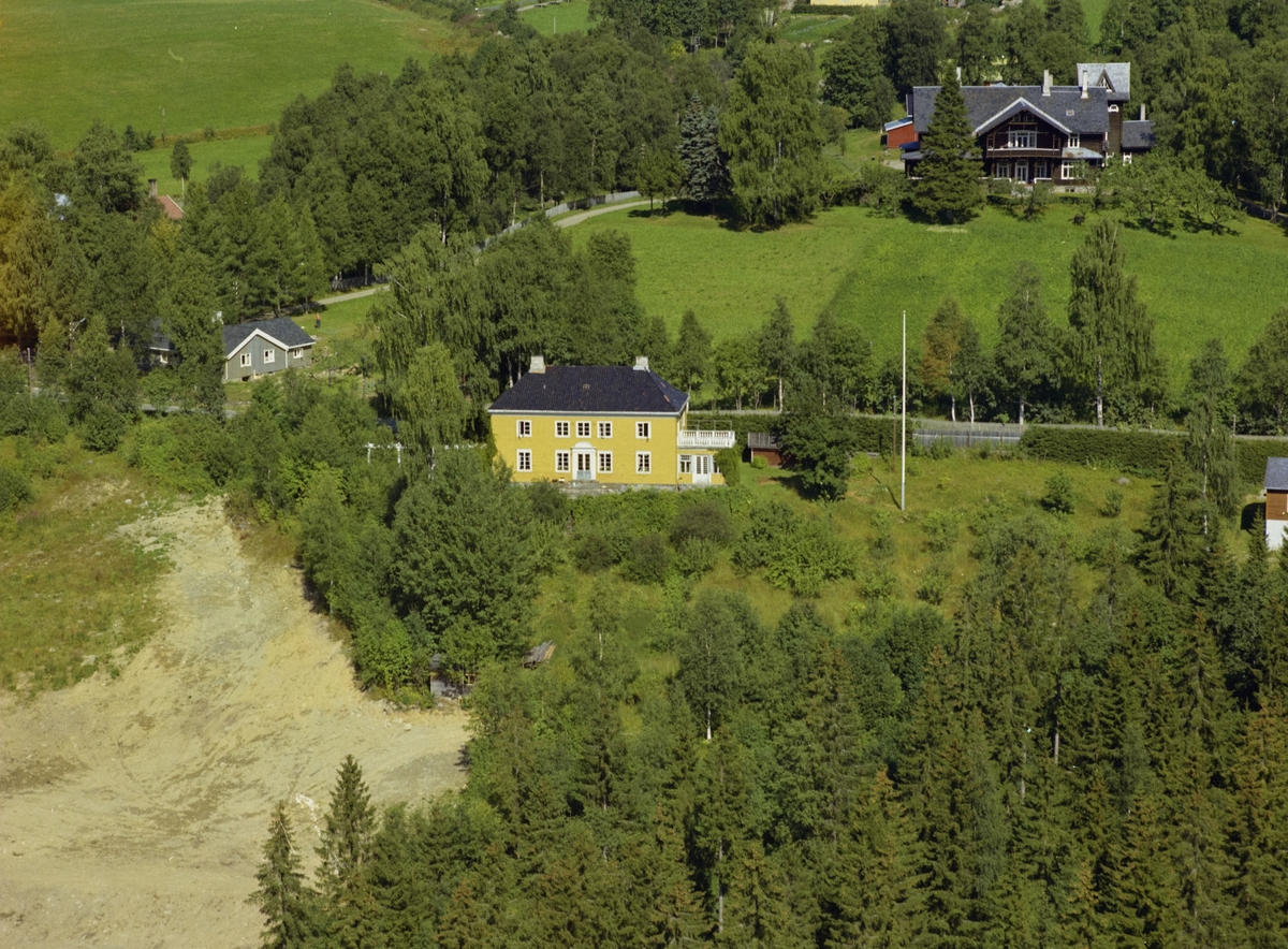 Stor gul villa bygd av fru Wiegaard, Granheim. Hage med busker. Granskog rundt. Kornhaug bak i bildet