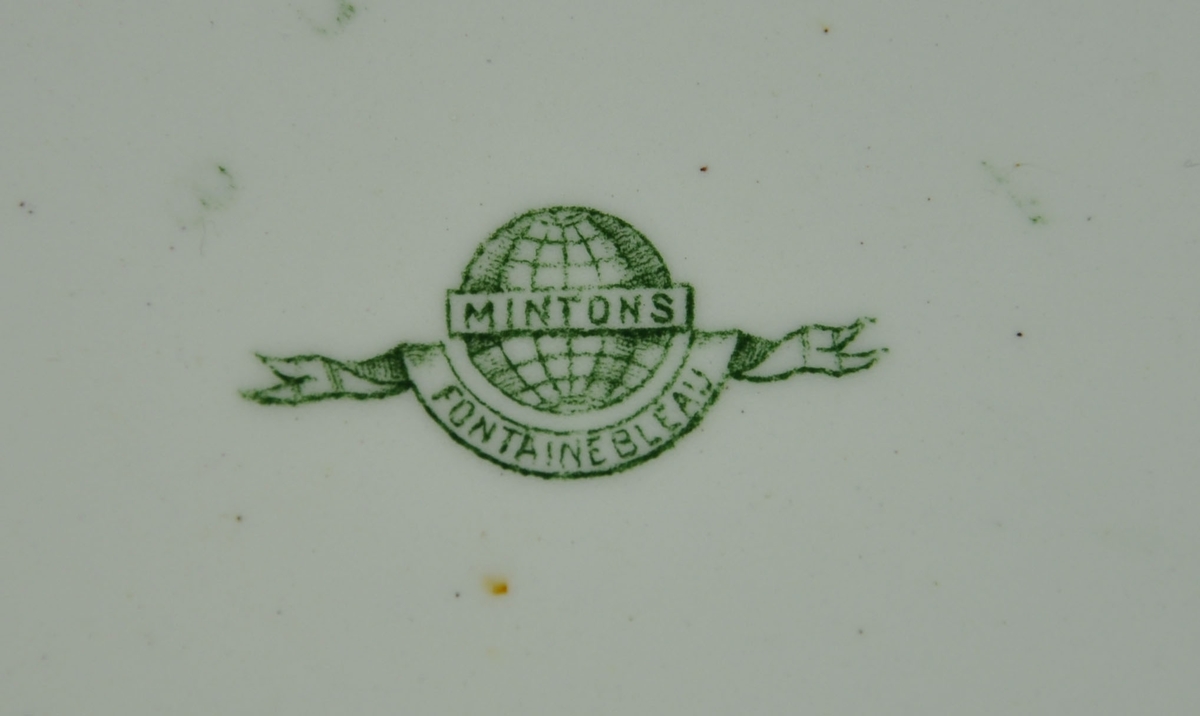 Rund tallerken av keramikk, steingods, med grønn bord. Borden består av eikekrans og guirlandere.
Mønsteret heter Fontainebleau.