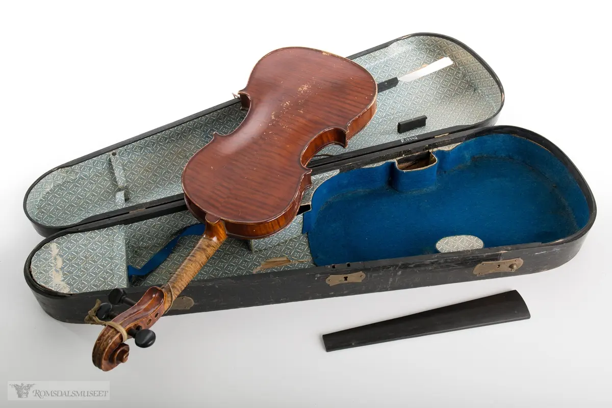 Brunlakkert fiolin. Mangler bue og strenger og fingerbrettet er løst.
Mest sannsynlig en kopi av en Stradivarius fiolin fra 1800- tallet, en såkalt "tyskerfele" eller "dusinfele".
(Se opplysninger for mer informasjon)

Svart fiolinkasse kledd med dekorert papir og kledd med blå filt i bunnen. Et lite rom i forkant for div. ekstrautstyr. Utstyr med lukkemekanisme foran og bak, og lås i messing. Håndtak av messing på toppen av kassen.