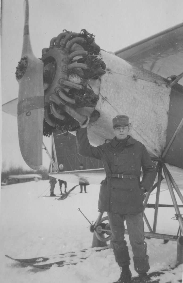 Porträtt av värnpliktig man vid nosen på flygplan S 6 med skidor, vintertid.
