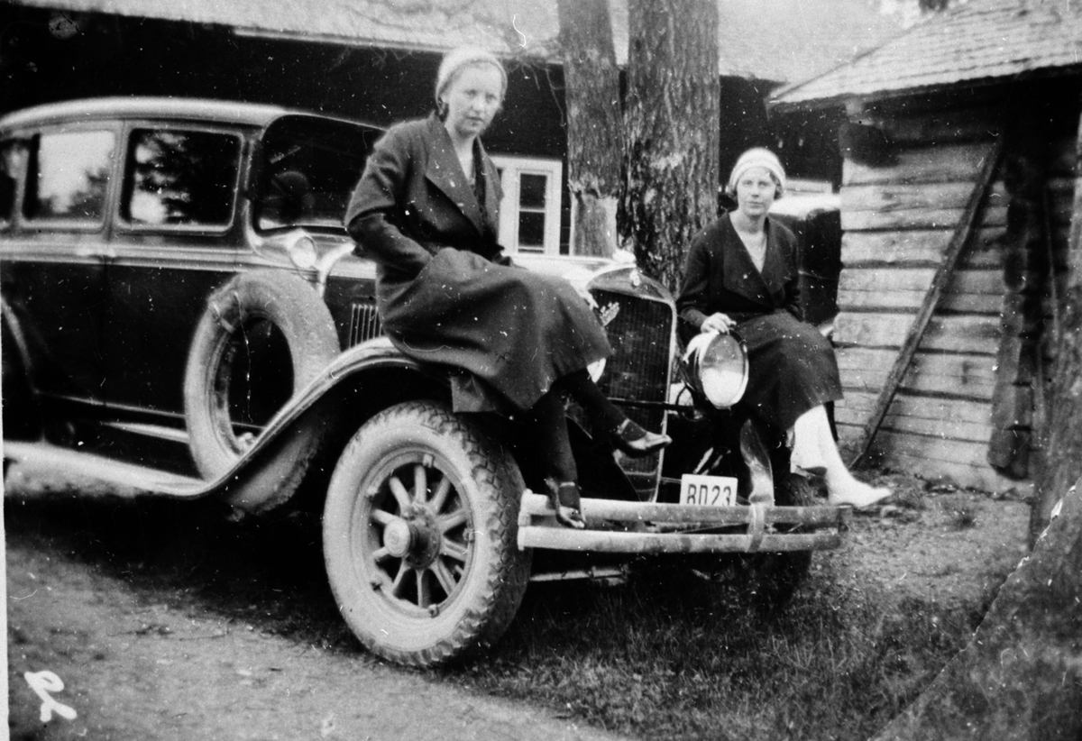 Två kvinnor som sitter på en bils motorhov.