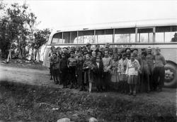 Gruppebilde av skoleunger, oppstilt foran en buss.