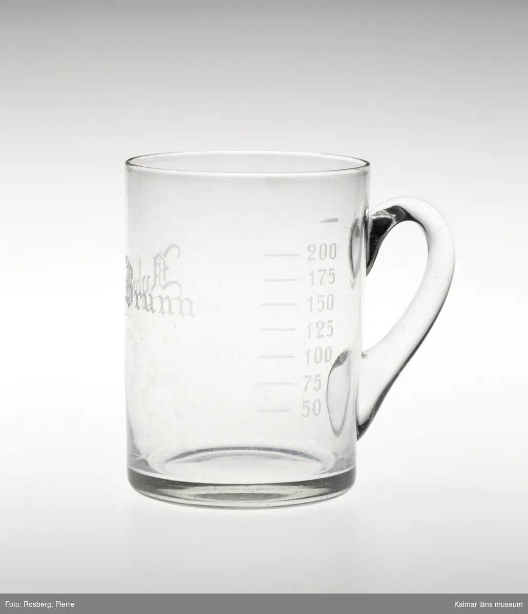 KLM 34599:1 Hankglas, av glas. Brunnsglas för Nybro Brunn och badanstalt, grundad 1883. Rakt glas med lodrät grepe. Något kupad botten. Graverad text och måttgradering, 50, 75, 100, 125, 150, 175, 200. Text: Nybro Brunn.