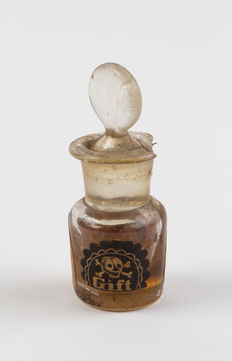 Liten gjennomsiktig medisinflaske med slepen glasskork.
Et giftmerke