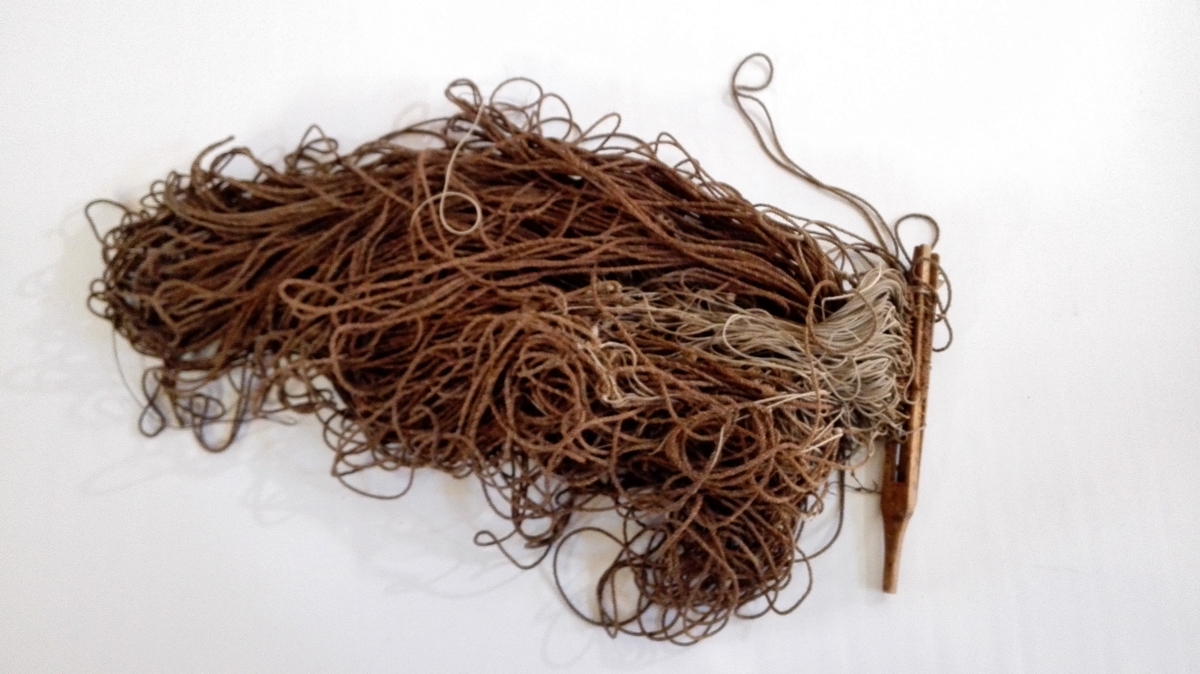 Line av brun hampetråd med forsyner av lys bomullstråd. Anglane er rusta og festa på ein spesiallaga haldar av tre, med handtak.