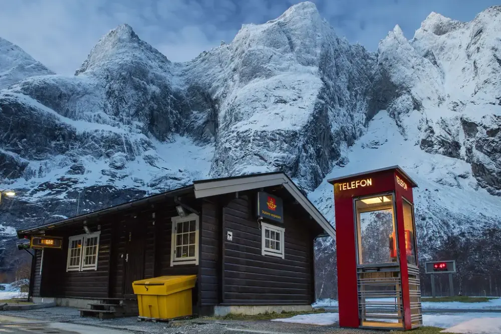 Rød telefonkiosk ved fjell og hus fra vegvesenet