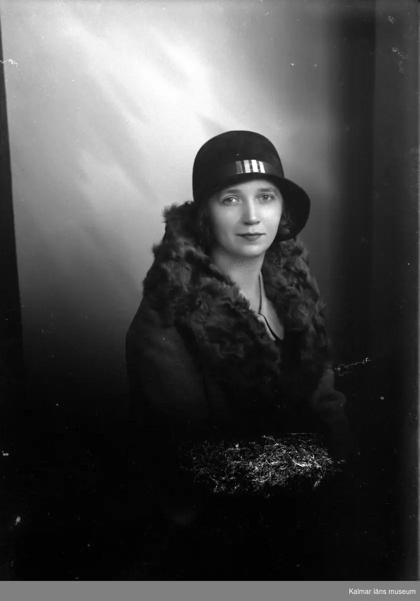 Ateljébild på en kvinna i hatt och i kappa med pläskrage. Beställare till bilden: Fröken Åström ifrån Kalmar.