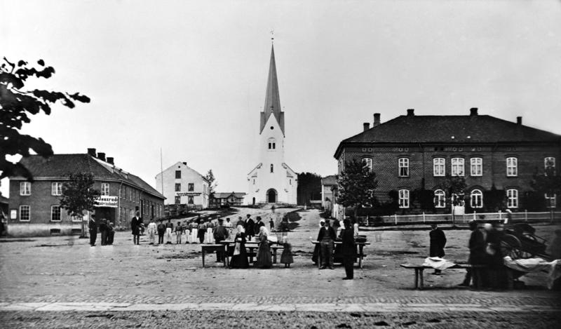 Historisk foto av Hamar domkirke med en menneskegruppe foran og bebyggelsen på begge sider av Kirkebakken.