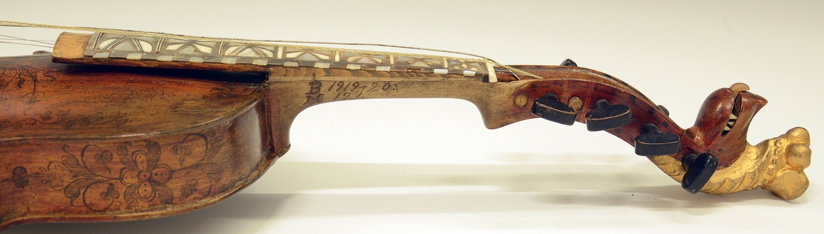 Fra protokollen: Hardingfele av den eldre, smale typen. Bruleggjingi stjerneforma, raud ferniss, stillepinnar og hovud spm vane (Hovudet nygylt). Paa merklappen inni stend: Fabrikeret af Erik Johnsen Helland i Bøe 1838. (Aarstalet ber merke av aa vera retta, serleg seinste siffer; papiret under aarstalet er vekkskrapa og talet uppnya paa berre treet.). Lok av gran, trojsk av hegg, botn av svartor, hovud av bjørk.