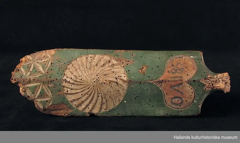 Klappträ som saknar handtag. Föremålet är dekorerat med utskärningar i form av en karvsnittsrosett. Målat i grön bottenfärg med detaljer i rött och gråvitt. Märkt med årtal och monogram 1857 OA, inom en hjärtform.