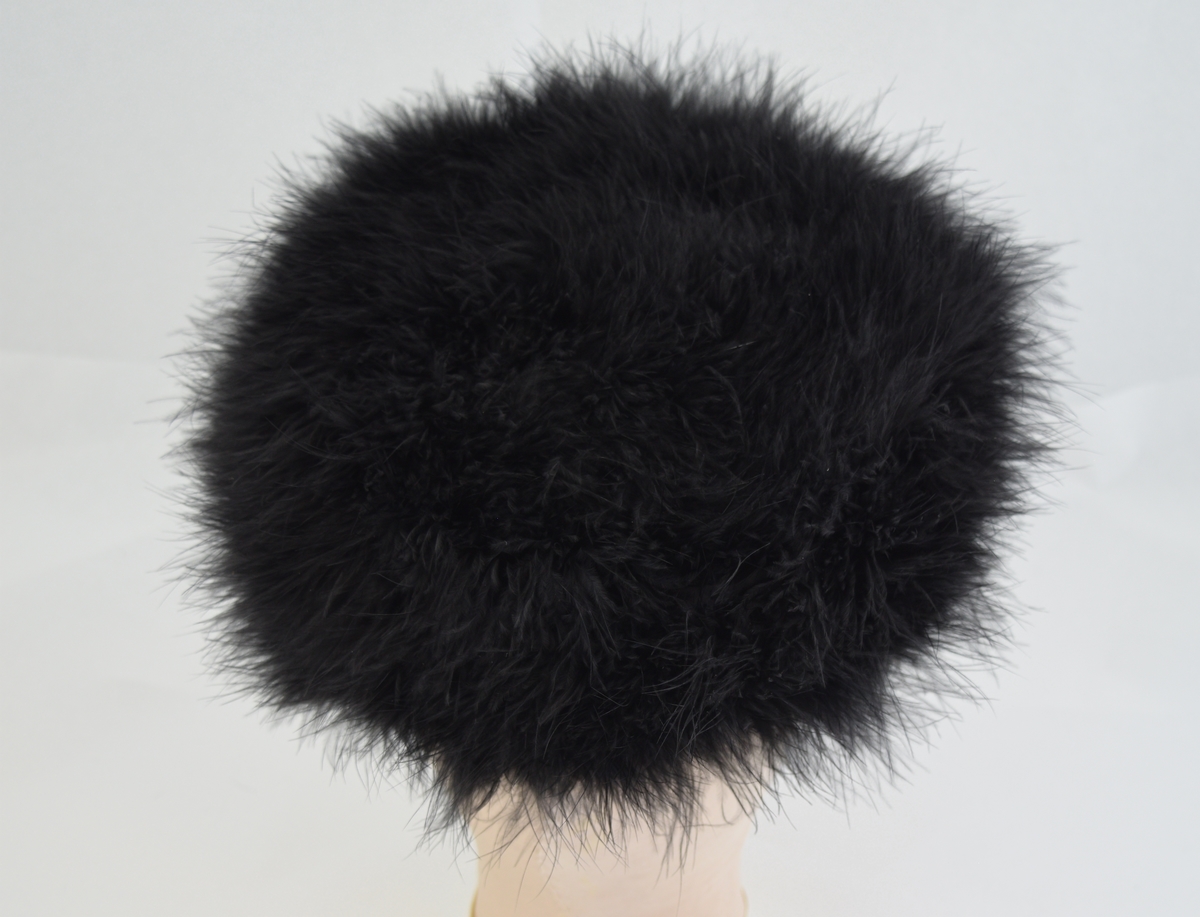 Rund ensfarget hatt med utside av lange tynnne dun. Foret med mørkt og blankt stoff.  Form: sirkulær m/ kant.