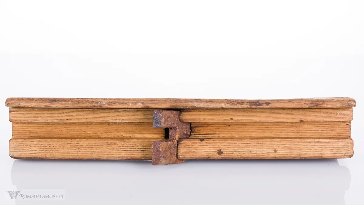 Rektangulær høvelstokk med buet overside med tilskåret høvelhorn, gaffelformet jern med kile og såle med spor for høvling av fjær.