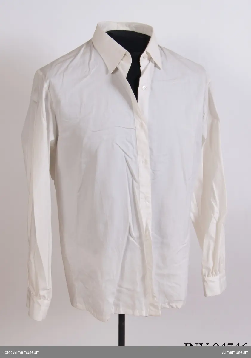 Vit skjorta i bomullstyg med plastknappar.
Etikett i nacken: "Creation Eaton, M 38, made in Sweden, 100 % cotton, tvättråd".