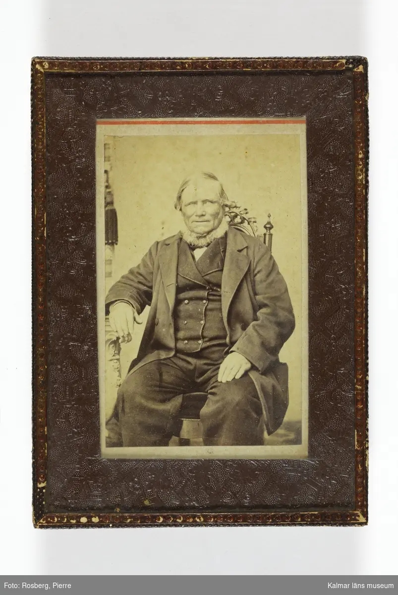 Porträtt av sjökapten N P Löfström med skägg, skepparkrans. Han sittande på en stol, hans högra arm vilar på ett bord.