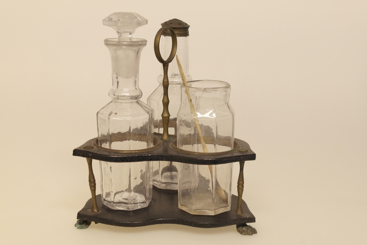 Kryddersett bestående av stativ (a), tre glass (b-e) og skje (f).
A) Krydderstativ av løvtre og støpt messing. Stativet er saget, høvlet, pusset og lakket. Messingkant rundt tre sirkelåpninger. Balusterformet håndtak med ring i messing i midten av stativet. Tre messingbein formet som dyreføtter.
B) Støpt glass med glasspropp (E)
C) Støpt glass med gjennomhullet messingkork
D) Støpt glass
F) Skje i bein som er skåret og pusset