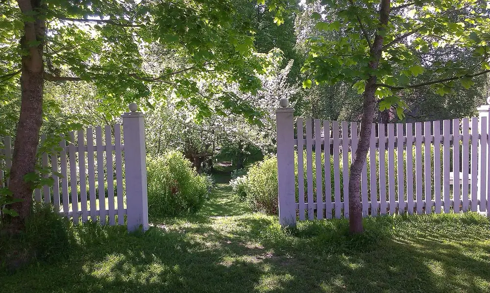 En hvitmalt, åpen hageport og en vakker grønn hage bakenfor. På amtmannsgården Steinberg, Toten, Norge.