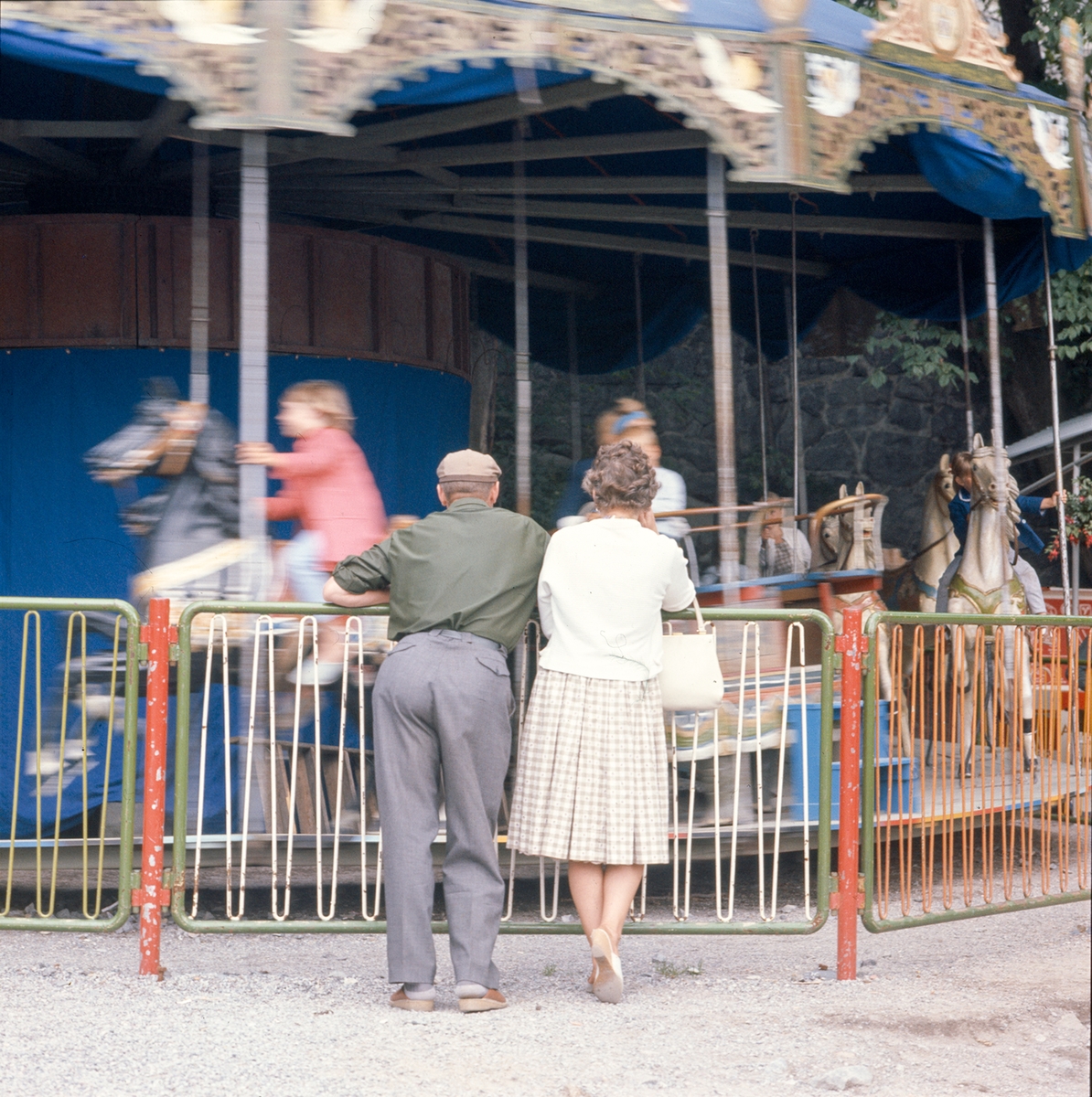 Ett äldre par betraktar barn som åker karusell.