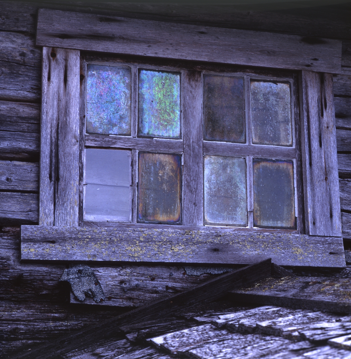 Fönster på en fäbod. Fönterspröjsen är av trä och rutornas glas har förändrats genom åren och skiftar i olika nyanser. Här syns också en del av takspånen. Färilaby väster om Ängratörn i Degerkölsvallen, 3-4 september 1991.