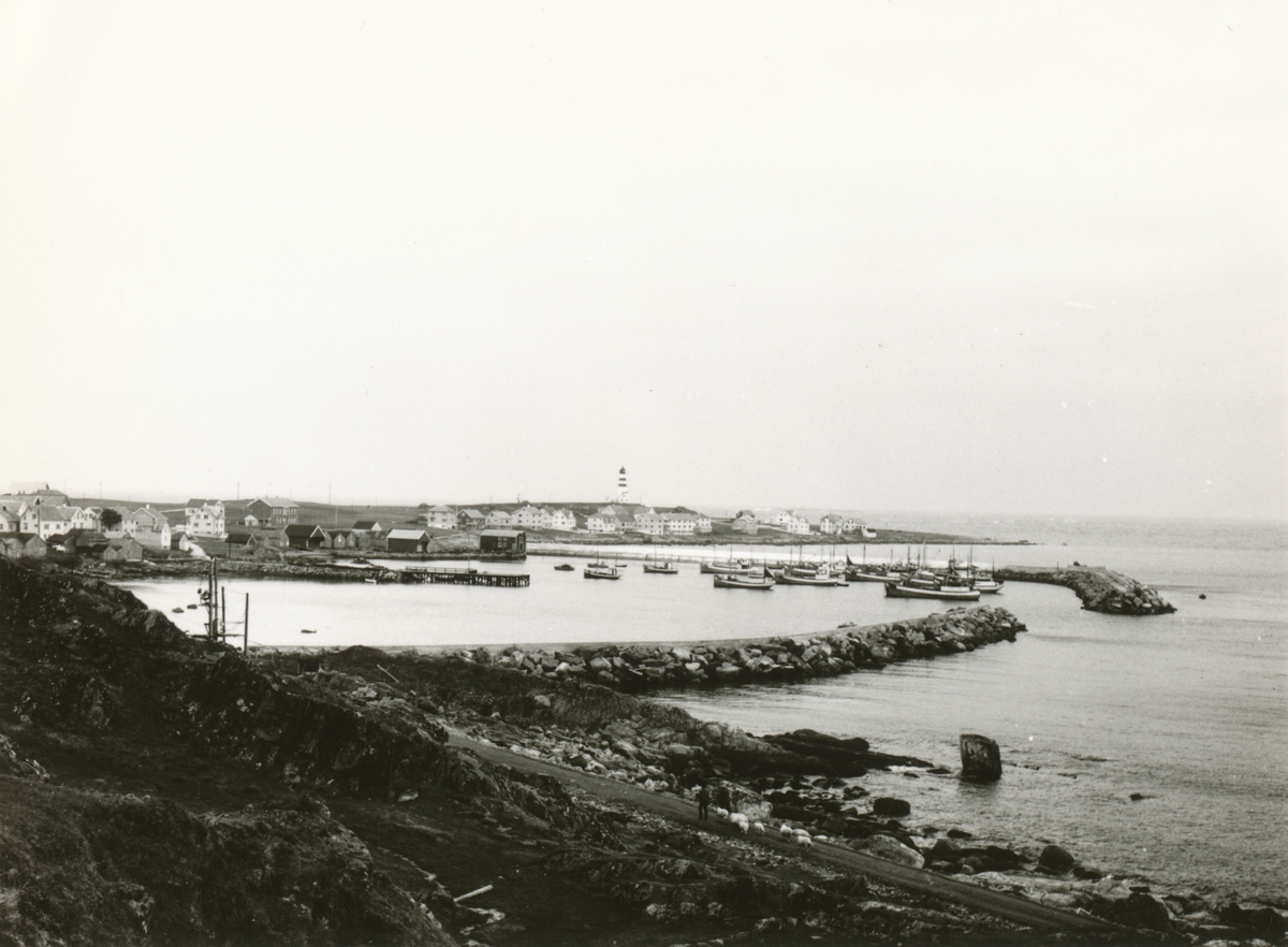 Prospektfotografi med oversikt over havna og bebyggelsen med fyrtårnet på Alnes, Godøy.
